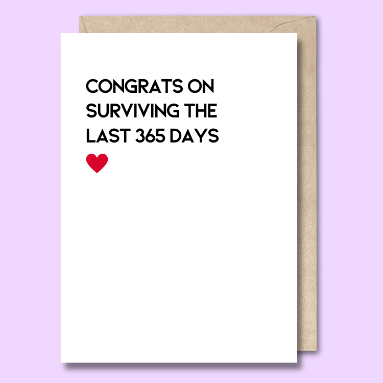 Front of a plain white greeting card with a picture of a tired cartoon giraffe leaning against a baby’s bottle. The text says "Congrats on surviving the last 365 days"