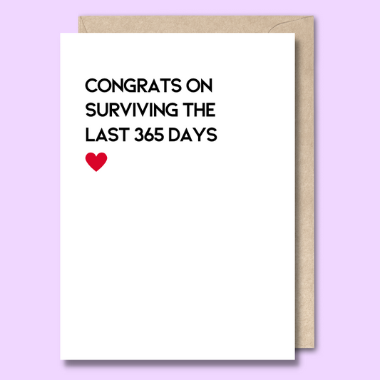 Front of a plain white greeting card with a picture of a tired cartoon giraffe leaning against a baby’s bottle. The text says "Congrats on surviving the last 365 days"